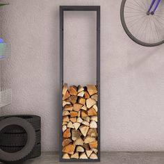 a stack of firewood in front of a wall with a bike tire on it