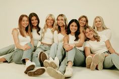 a group of women sitting next to each other on top of a white floor with their legs crossed