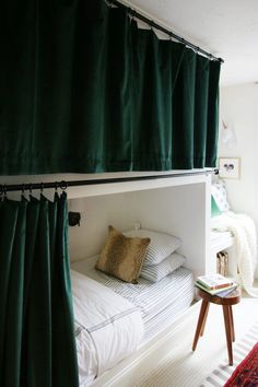 a bunk bed with green curtains hanging from it's sides and pillows on the bottom