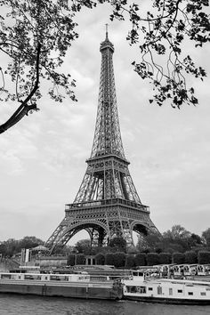 the eiffel tower in black and white with boats on the river below it