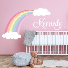 a baby's room with a crib, teddy bear and rainbow wall decal