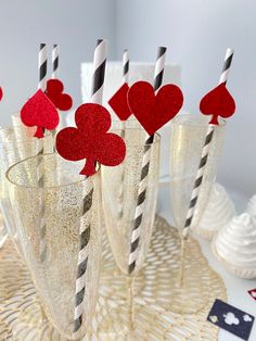 four glasses with straws and paper hearts in them sitting on a table next to cards