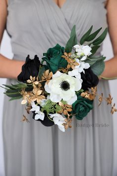 a woman in a gray dress holding a white and black bouquet with green leaves on it