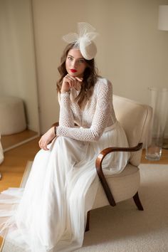 a woman in a white dress sitting on a chair with her hand under her chin