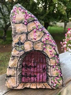 a stone house with pink flowers painted on it's front and side door is sitting on a wooden fence