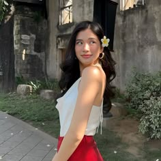 a woman in a white top and red skirt posing for the camera with a flower in her hair