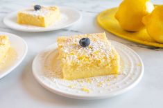 three slices of lemon cake on plates with blueberries and lemons in the background