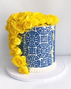 a blue and white decorated cake with yellow flowers on the top, in front of a white background