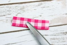 a pink and white checkered ribbon next to a pair of scissors on a table