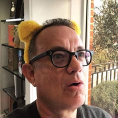 a man wearing glasses and a yellow cat ears headband is looking at the camera