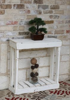 a small white table with a potted plant on top and some rocks under it