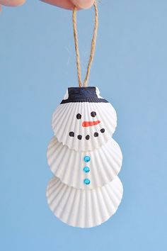 a snowman ornament hanging from a string on a blue background with a hand holding it