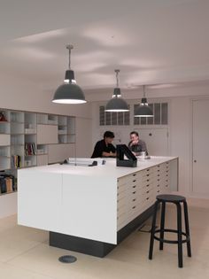 two people sitting at a counter in a room with bookshelves on the wall