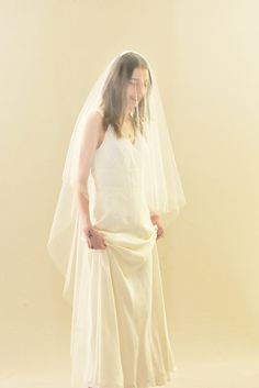 a woman in a white dress is wearing a veil over her head and standing with her hands on her hips