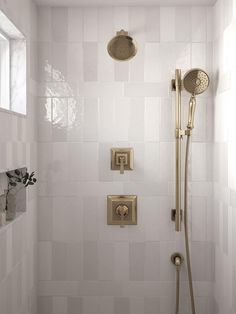 a shower head and hand shower in a white tiled bathroom with gold fixtures on the wall