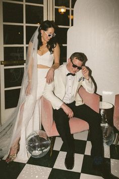 a bride and groom sitting on a pink chair in front of a large white wall