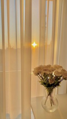 a vase filled with white flowers sitting on top of a table next to a window