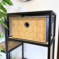 a black shelf with a wooden box on top and plants in the corner next to it