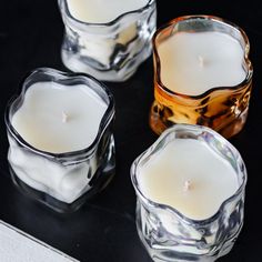 three glass candles sitting next to each other on a black counter top with one lit candle in the middle