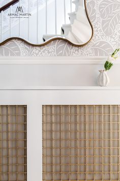 a mirror and vase on top of a white door with decorative wallpaper behind it