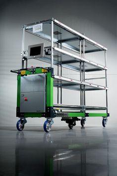 a green and black cart with several shelves on it's wheels in front of a gray wall