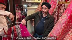 a man standing in front of some red and pink sari on display at a store