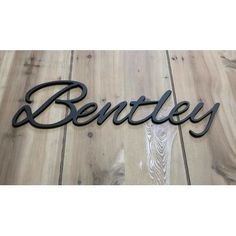 the name bentley is made out of metal and sits on a wooden floor with wood planks