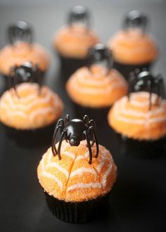 cupcakes with spider decorations on them sitting on a black table top, ready to be eaten