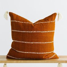 a brown and white striped pillow with tassels on the bottom, sitting on a wooden shelf