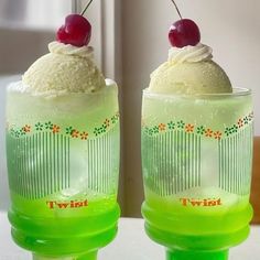 two green cups with ice cream and cherries on the top one has a cherry in it