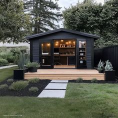 a small black shed with an outdoor bar in the back ground and landscaping around it