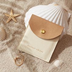 a white shell with a tan leather card holder and two gold rings laying on the sand