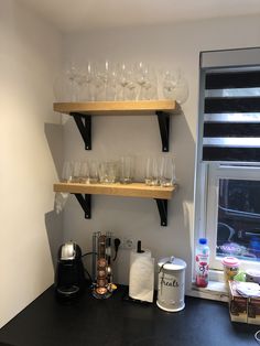 two wooden shelves holding glasses and cups on a black counter top next to a window