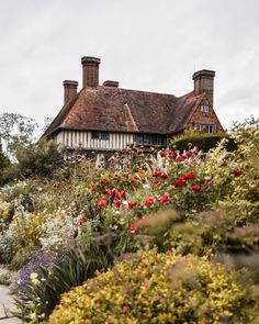 an old house surrounded by colorful flowers and greenery