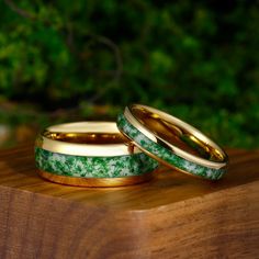 two wedding bands with green flowers on them sitting on top of a wooden table in front of some trees