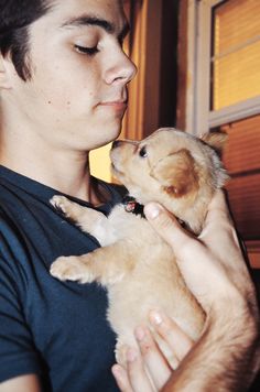 a man holding a puppy in his arms and kissing it's face with its eyes closed