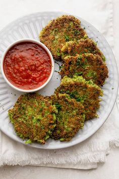 broccoli fritters on a white plate with a small bowl of tomato sauce