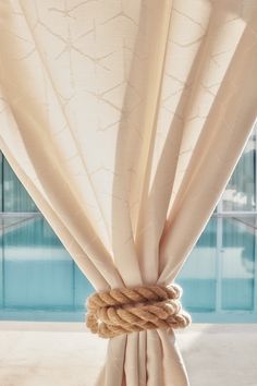 a rope wrapped around the top of a curtain next to a swimming pool with water in the background