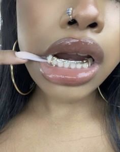 a woman brushing her teeth with an electric toothbrush in front of her face and wearing gold hoop earrings