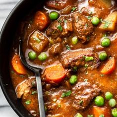 beef stew with carrots, peas and potatoes in a black bowl on a white table