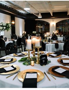 the table is set with black and gold place settings, white linens, and candles