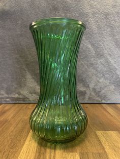 a green glass vase sitting on top of a wooden table next to a gray wall