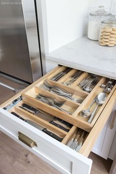 an open drawer with utensils and silverware in it on a kitchen counter