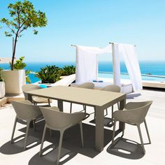 an outdoor dining table and chairs on a deck overlooking the ocean with white drapes