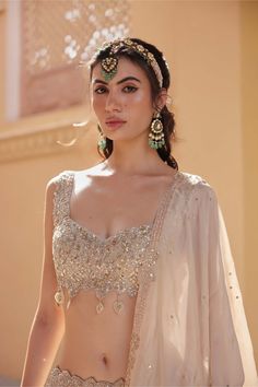 a woman in a bridal outfit with jewelry on her head and hands behind her back