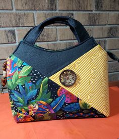 This fun handbag is made with fabrics from Laurel Burch Jungle Songs, and Tula Pink, the Free Spirit collection. Really fun fabrics to work with and to carry in a darling tote bag!  Just the right size for everyday going about your day with plenty of room for your necessities. The outside slip pocket is the perfect place to stash your phone, easy to grab when that important call comes in! Inside there are two more slip pockets on one side and a large zipper pocket on the other side!  It's such a great looking bag, with the asymmetrical pocket on the front and the beautiful large wood cut out button as the focal point! The Jungle Song fabric covers the back and interior facings, and the Tula Pink orange stripe makes the interior bright and light, easy to find all of your treasures! It close Fun Handbag, Fun Fabrics, Wood Cut, Laurel Burch, Tula Pink, Gorgeous Bags, Handle Bag, Fabric Covered, Free Spirit