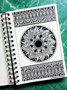 an open notebook with black and white designs on the cover, sitting on a green marble surface