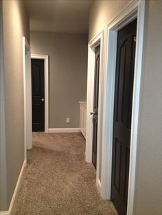 an empty hallway with two black doors and white trim on the walls, leading to another room