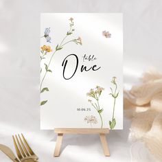 a table sign with flowers on it next to a fork