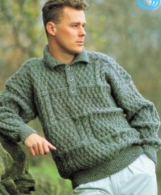 a man in a green sweater leaning against a rock with his hand on his hip